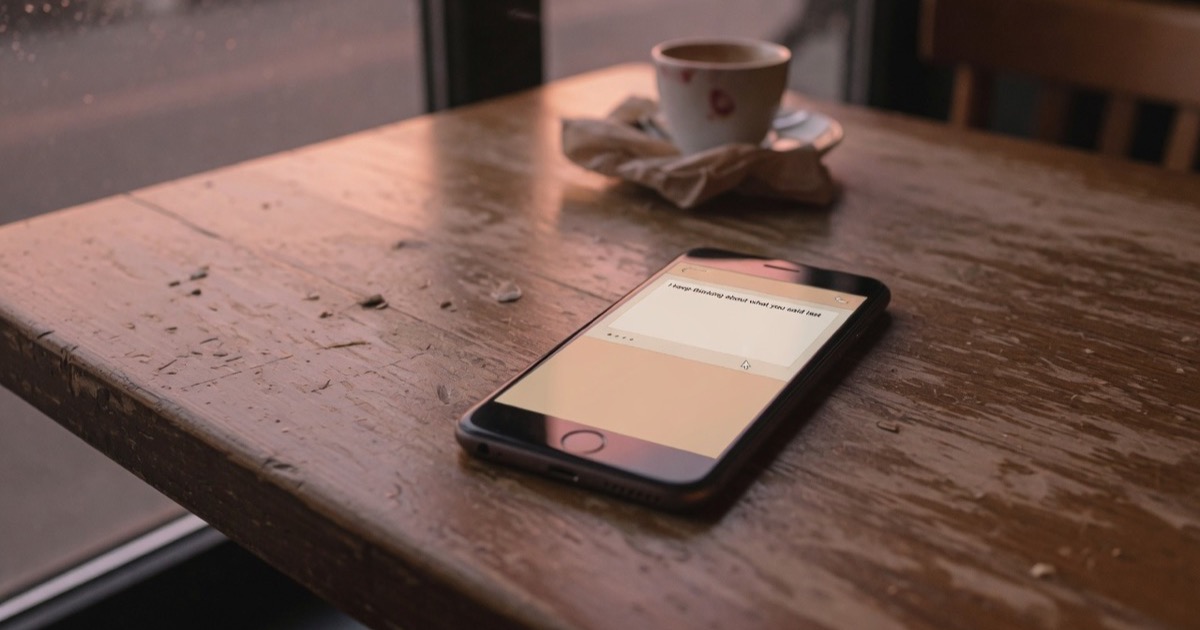Un celular boca arriba sobre una mesa de madera de café, con la pantalla encendida al atardecer y un mensaje de texto a medio escribir.
