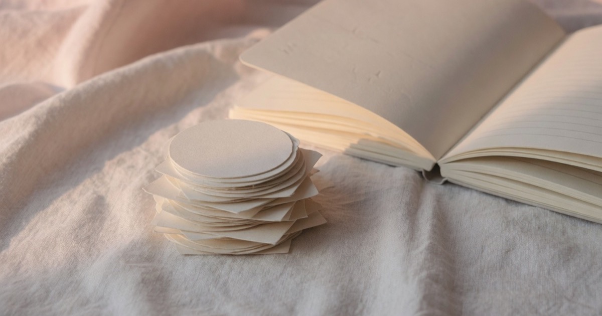 A small stack of plain paper tokens on pale linen, next to an open notebook.
