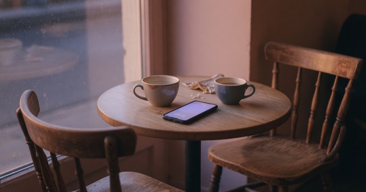 Deux chaises vides face à face autour d'une table de café, avec un téléphone qui s'allume doucement entre deux tasses.