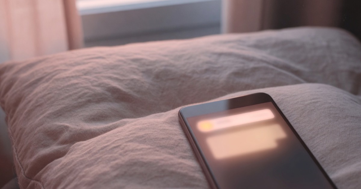 Un teléfono boca arriba sobre un sofá de lino, con la pantalla iluminada por una notificación, luz cálida de atardecer entrando por la ventana.